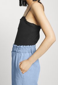 Černý žebrovaný top s volánovými okraji, zkombinovaný s světle modrými, volnými kalhotami s elastickým pasem a bočními kapsami.