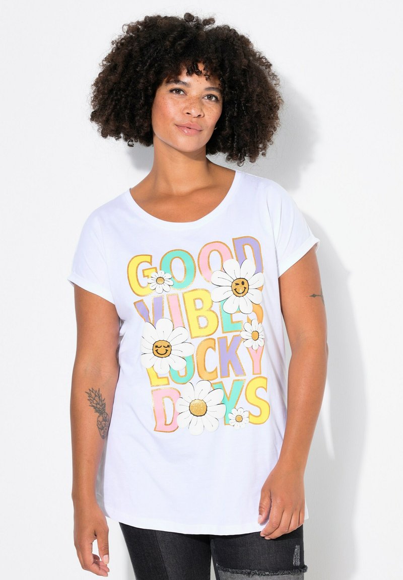T-shirt blanc à manches courtes avec un graphique coloré portant le texte "BONNES VIBRATIONS JOURS FÉLICES" et des marguerites souriantes dans un design ludique.