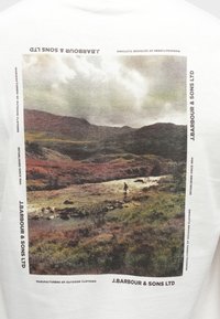 Biały bawełniany t-shirt z wyblakłym nadrukiem krajobrazu przedstawiającym pagórki i rzekę z osobą wędkarską. Logo marki i tekst w czerni po bokach.