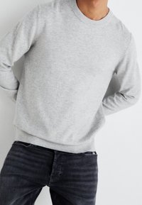 Sweat-shirt gris clair à col ras du cou en mélange de coton, avec poignets et ourlet côtelés, porté avec un jean en denim foncé. Texture lisse, coupe décontractée.