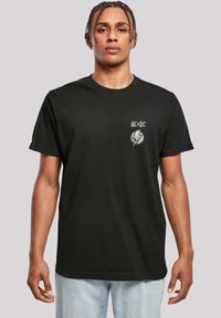 Black cotton t-shirt with short sleeves, featuring a grey AC/DC logo and lightning bolt design on the left chest area. Casual fit.