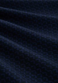 Tessuto blu scuro con un sottile motivo geometrico. Il materiale appare morbido con una superficie texturizzata, che mostra pieghe e avvolgimenti.