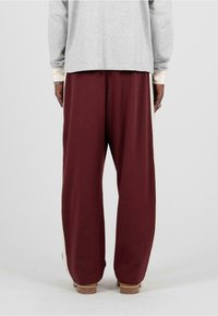 Bordové nohavice s širokými nohavicami a hladkou textúrou, s kontrastnými svetlými bočnými pruhmi. Nosené s dlhým šedým topom, ktorý má jednoduchý dizajn.