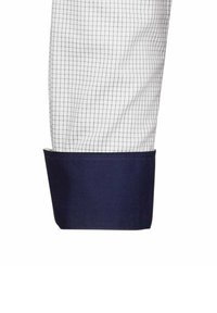 Camicia bianca con un piccolo motivo a quadri neri, con polsini blu navy. Il tessuto appare liscio con una finitura pulita e un design strutturato.