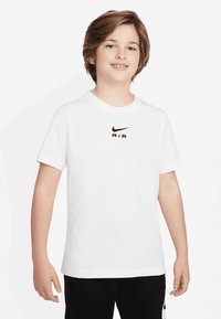 T-shirt bianco in cotone con logo Nike nero e la parola "AIR" sotto. Maniche corte e scollo rotondo, abbinato a pantaloni neri.