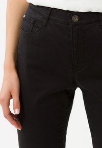Pantaloni neri in misto cotone con cinque tasche; presentano una chiusura frontale con bottone e passanti per cintura. Tessuto liscio, design a gamba dritta.