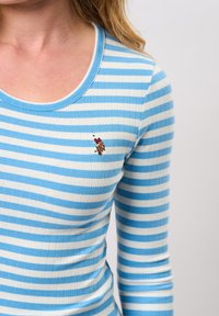 Lys blå og hvit stripete langermet topp, ribbet tekstur, med rund hals og liten brodert detalj på brystet.