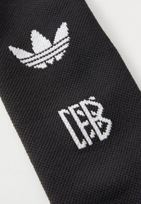 Zwarte stof met een witte Adidas trefoil logo en de tekst "LEFB" in geweven detail. Gestructureerd oppervlak met contrasterende graphics.