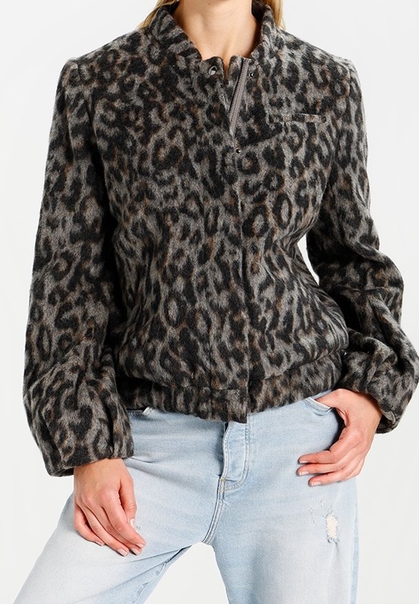 Cappotto in stampa leopardata con texture morbida e pelosa. Presenta un alto colletto, chiusura con zip e maniche a palloncino. Indossato con jeans strappati di un blu chiaro.