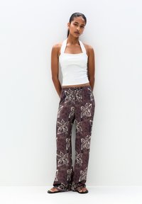 Top bianco con spalline abbinato a pantaloni marroni a fantasia con motivi floreali. L'outfit è completato da infradito nere.