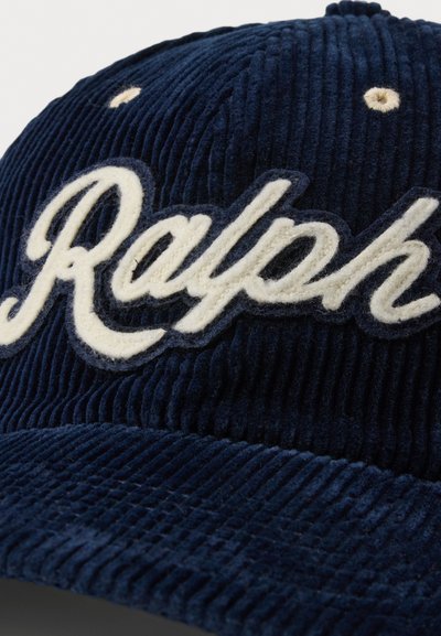 Jūras spēku korduroja cepure ar baltu izšūtu tekstu "Ralph" priekšpusē, ar teksturētu virsmu un apaļu ventilācijas caurumu augšpusē.