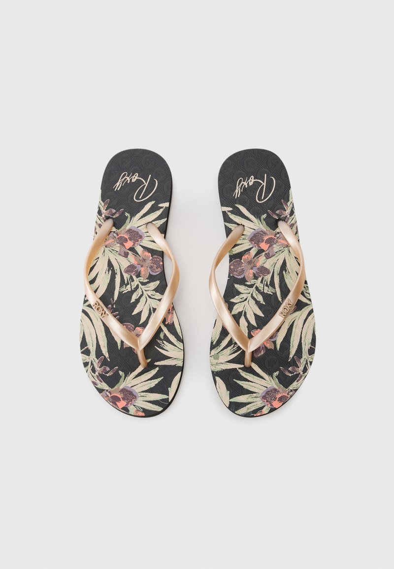 Paire de tongs noires avec motif floral et brides beige, logo de la marque visible sur la semelle intérieure et la bride, posées sur un fond clair.