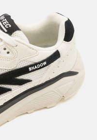 White and black sneaker with mesh and suede upper, featuring a textured sole and "SHADOW" branding on the side. Rounded toe design.