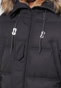 Czarna pikowana kurtka puchowa z kapturem podszytym sztucznym futrem, z dwoma przednimi kieszeniami, srebrnymi elementami metalowymi i sznurkami przy dekolcie.