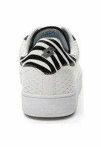 Sneaker bianco con materiale testurizzato, tacco a strisce zebrate bianche e nere, e un design minimalista. Presenta un piccolo logo argentato sul retro.