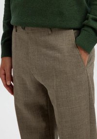 Brune, strukturerede bukser lavet af letvægtsstof, med sidelommer og en skræddersyet pasform, parret med en mørkegrøn, strikket sweater.