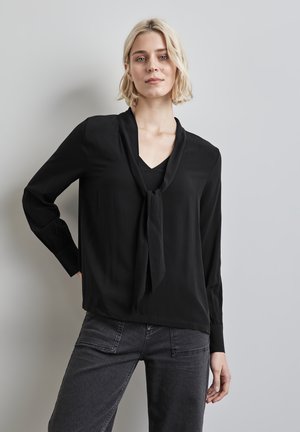Blusa nera con maniche lunghe e dettaglio a fiocco sul collo. Realizzata in tessuto morbido. Abbinata a pantaloni grigio scuro con tasche.