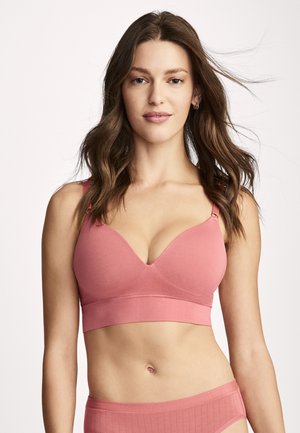 Woman with long brown hair wearing matching pink bra and high-waisted underwear, facing forward against a plain light background.