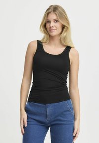 Top nero senza maniche con un design aderente, scollatura rotonda e una texture morbida. Abbinato a jeans blu con un taglio classico e tasche anteriori.