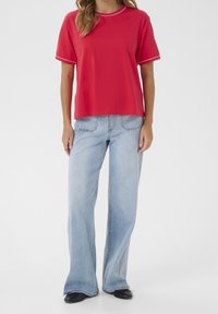 Red t-shirt with a round neckline and white trim, paired with light blue wide-leg jeans and black shoes, featuring a relaxed fit.