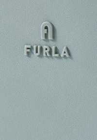 Gaiši zila teksturēta virsma ar izspiestām burtiem, kas veido vārdu "A FURLA", ar gludu, matētu apdari un smalku graudu rakstu.