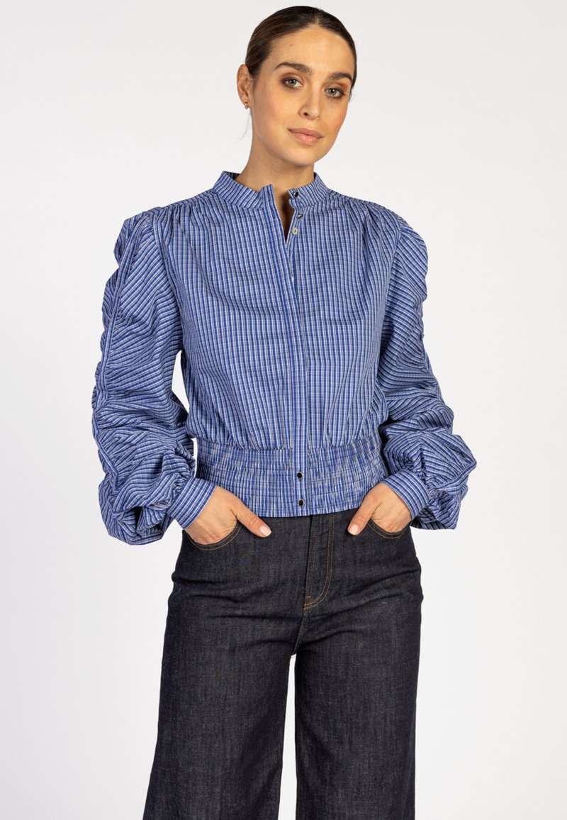 Blauwe en witte gestreepte blouse met pofmouwen, voorzien van een hoge kraag en knoopsluiting, gecombineerd met een donkere denim wijde broek.
