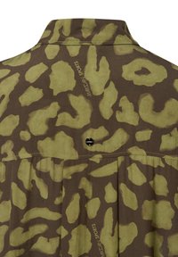 T-Shirt mit Camouflage-Muster in Grün- und Brauntönen, leichtes Material, Knopfdetail auf der Rückseite und Textbranding an der Seite.