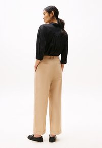 Camicia nera in lino con maniche a tre quarti, abbinata a pantaloni beige a vita alta e gamba larga e scarpe nere basse. Design semplice e pulito.