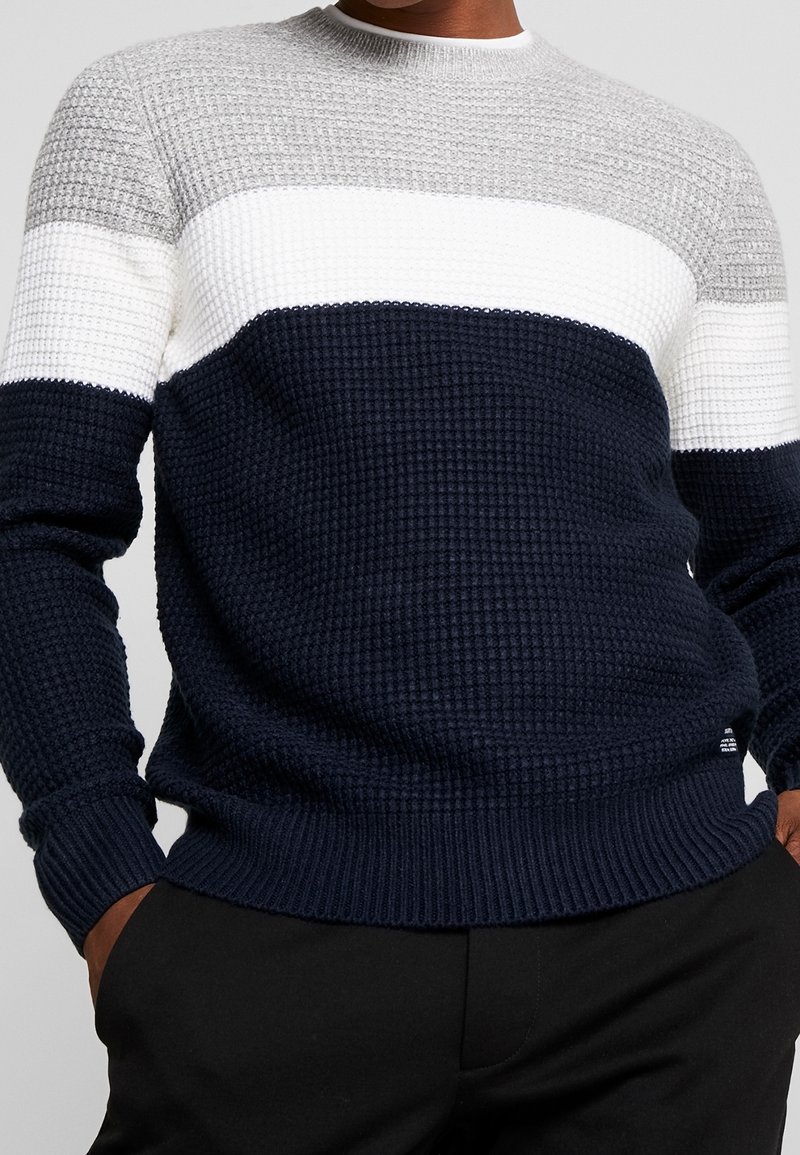 Knitted crewneck sweater featuring horizontal stripes in grey, white, and navy. Textured fabric with ribbed cuffs and hem.