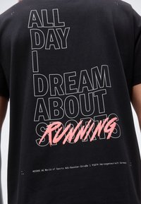 Μαύρο μπλουζάκι με λευκό κείμενο "ALL DAY I DREAM ABOUT" και ροζ γραφή "RUNNING" πάνω από τη λέξη "SPORTS" στην πλάτη.