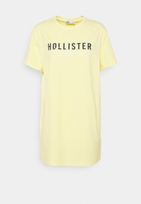 Żółta bawełniana koszulka z krótkim rękawem i okrągłym dekoltem, z czarno-białym nadrukiem "HOLLISTER California" z przodu.