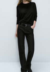Black long-sleeve shirt paired with dark wash straight-leg jeans, featuring a sleek belt with a silver buckle, against a light gray background.