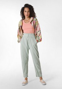 Gestreepte, kleurrijke oversized jas met puffy mouwen over een aansluitend roze tanktop; lichtgroene tapered broek en beige sneakers maken de outfit compleet.