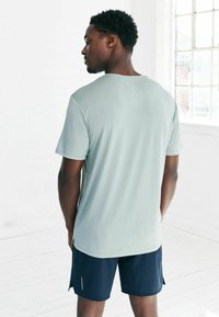 Mintgrünes, kurzärmeliges Sportshirt aus einem strukturierten Stoff. Kombiniert mit dunkelblauen Shorts mit seitlichen Schlitzen und reflektierenden Akzenten.