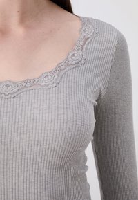 Grå stripete langermet topp med blomstermønster i kantene rundt halsen. Stoffet har en glatt tekstur og en tettsittende design.