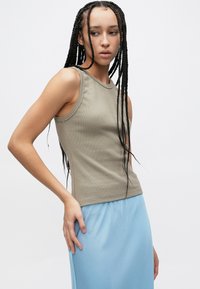 Top kaki din tricot cu model reiat, cu croială mulată și decolteu rotund, asortat cu o fustă vaporoasă de culoare albastru deschis. Detalii de material texturat vizibile.