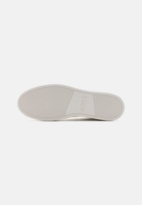 Semelle de sneaker blanche avec un motif texturé côtelé. Présente un logo embossé sur le côté, conçu pour l'adhérence et la stabilité.