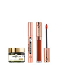 Ensemble de trois produits cosmétiques : un pot en verre vert avec un couvercle doré, un tube de mascara rose doré et un tube de rouge à lèvres liquide rose doré avec applicateur.