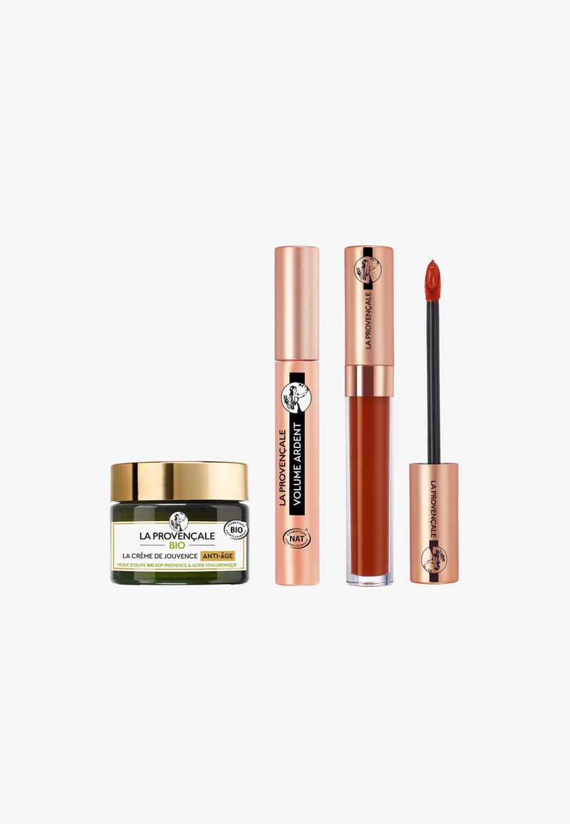 Ensemble de trois produits cosmétiques : un pot en verre vert avec un couvercle doré, un tube de mascara rose doré et un tube de rouge à lèvres liquide rose doré avec applicateur.