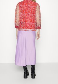 Blusa rossa floreale trasparente con maniche a sbuffo abbinata a una gonna maxi lavanda, completata da stivali neri con tacco al ginocchio.