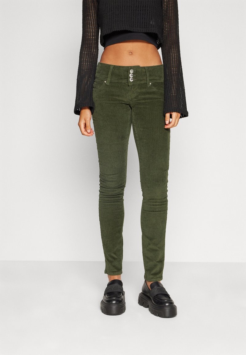 Green corduroy pants with a slim fit, featuring a four-button closure and front pockets. Paired with a black cropped sweater and platform shoes.