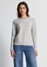 Lichtgrijze trui met lange mouwen, geribbelde manchetten en een ronde halslijn. Soepele textuur, gedragen met lichtblauwe wijd gesneden jeans.
