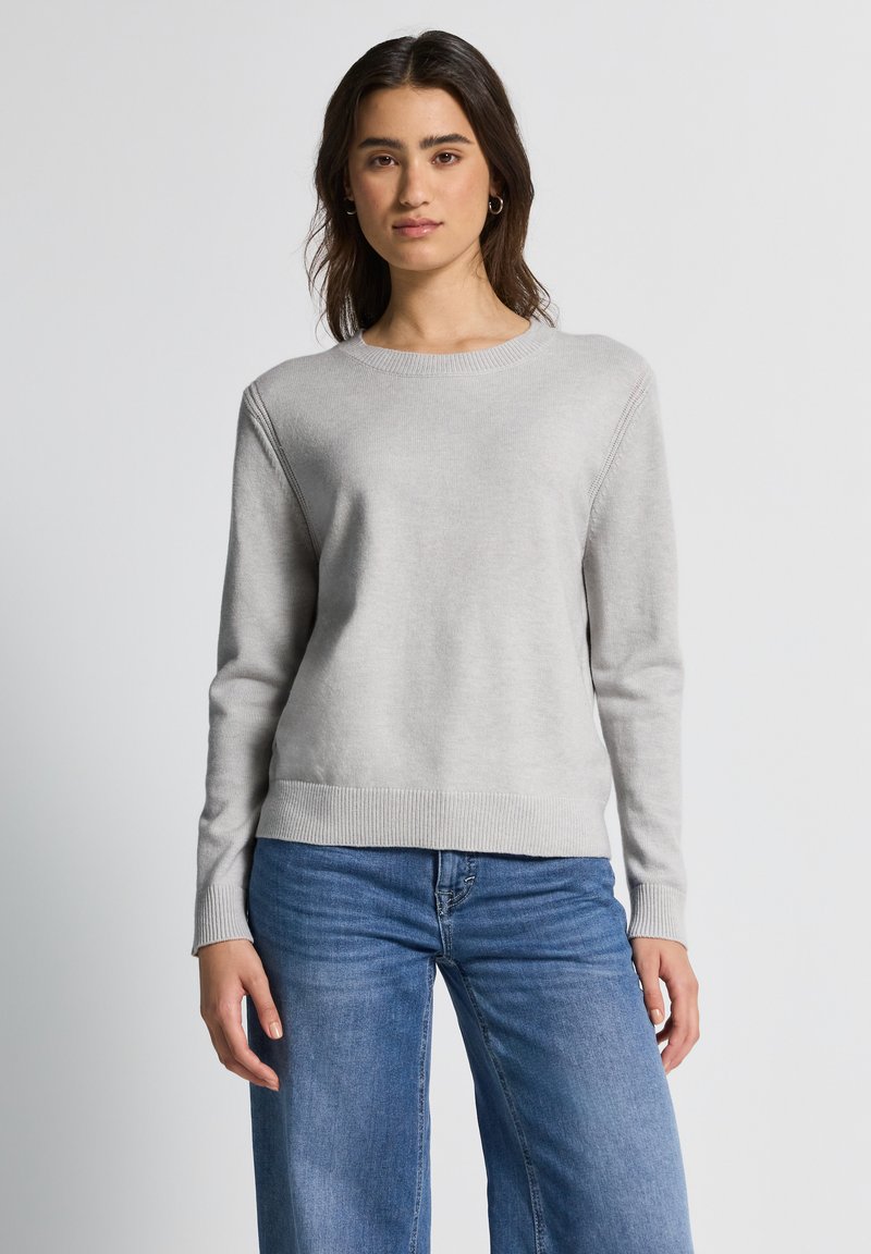 Lichtgrijze trui met lange mouwen, geribbelde manchetten en een ronde halslijn. Soepele textuur, gedragen met lichtblauwe wijd gesneden jeans.