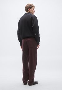 Hanorac negru cu tiv și manșete în rețea, asortat cu pantaloni largi bordo cu buzunar pe spate, purtați cu pantofi negri.