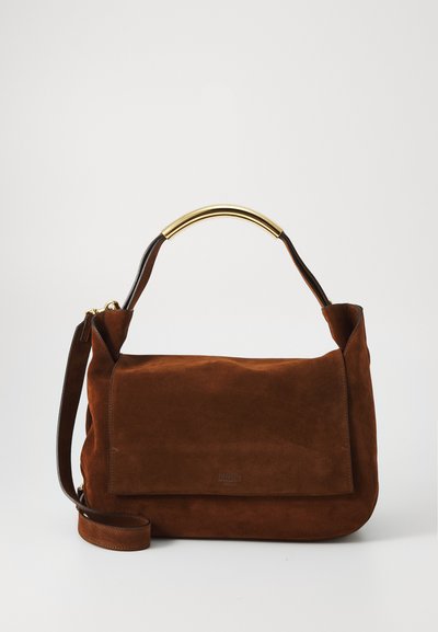 Brown suede handbag with a structured shape, featuring a gold-tone curved handle and a detachable leather strap. Minimalist design with a flap closure.