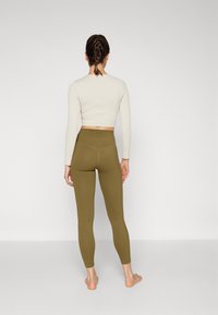 Olive green leggings with a high waistband, paired with a beige cropped long-sleeve top. Smooth texture, fitted design, no visible patterns.