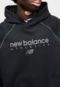 Zwarte capuchontrui met een grijs geborduurd "new balance"-logo en de tekst "ATHLETICS". Gemaakt van zachte, gestructureerde stof met een ontspannen pasvorm.