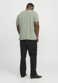 Mintgrønt kortærmet t-shirt med afslappet pasform, parret med sorte bukser og mørke sneakers. Glat stofstruktur og enkelt design.