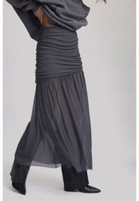 Jupe grise avec corsage froncé et bas fluide, transparent. Elle présente une texture lisse et un design superposé. Assortie à des bottines noires à talons pointus.