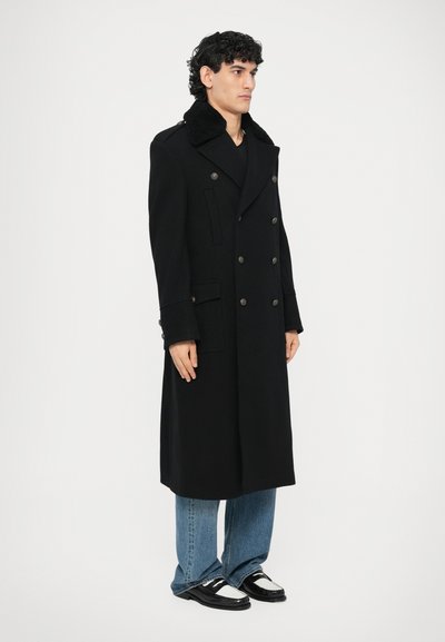 Abrigo negro de lana con doble botonadura y cuello alto, con botones de latón, bolsillos laterales y silueta recta. Combinado con vaqueros azul claro.